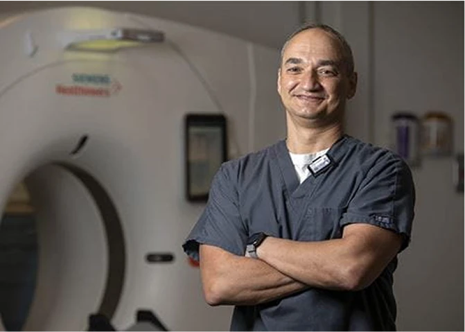 Eugene, a CT Technologist, standing in front of a CT scanner.