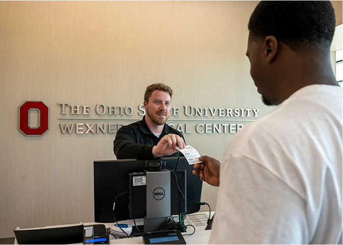 An employee handing a registration document to a patient in the medical center lobby.