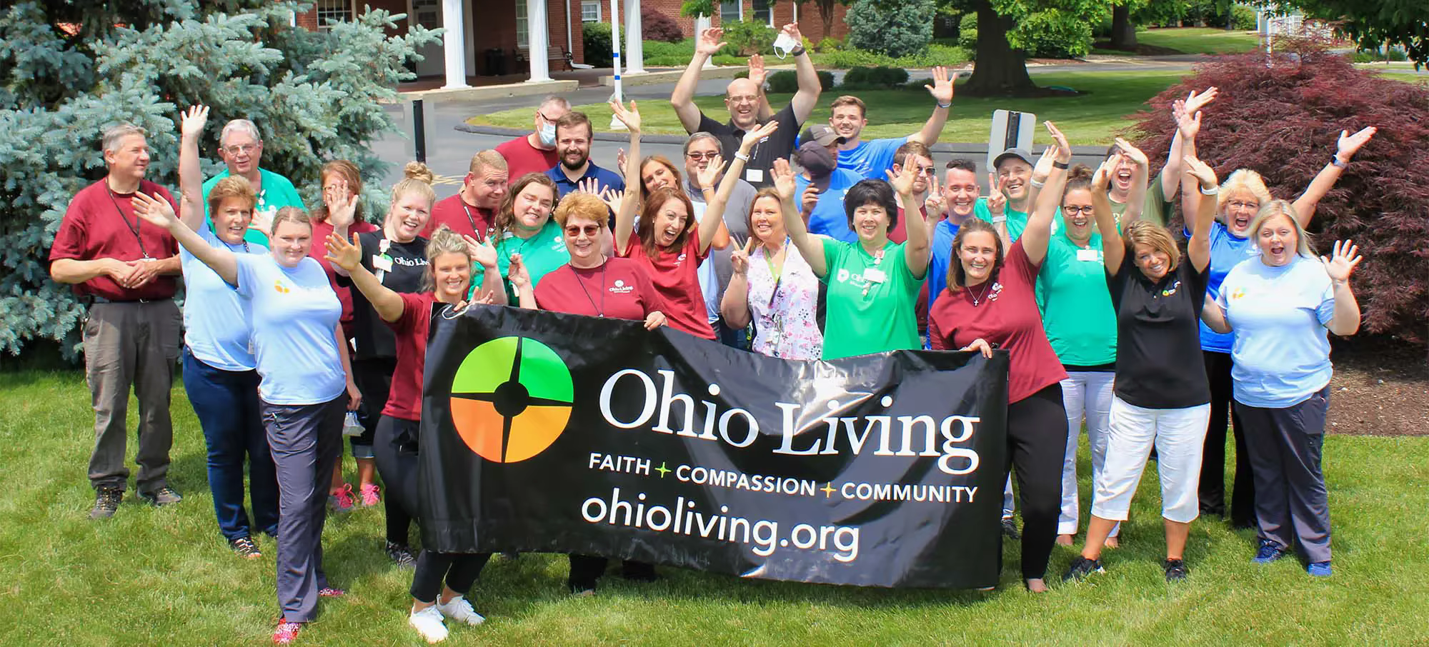 A large group of staff members stand outside a facility waving and holding an Ohio Living sign.