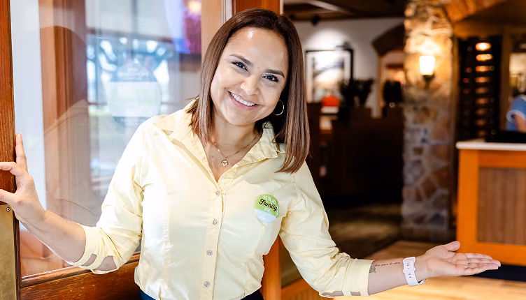 An Olive Garden host smiling and holding a door open.