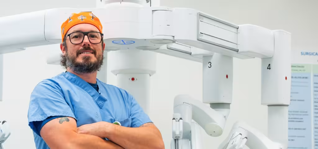 Smiling Phoebe doctor in a surgical cap and scrubs standing in front of a medical scanner.