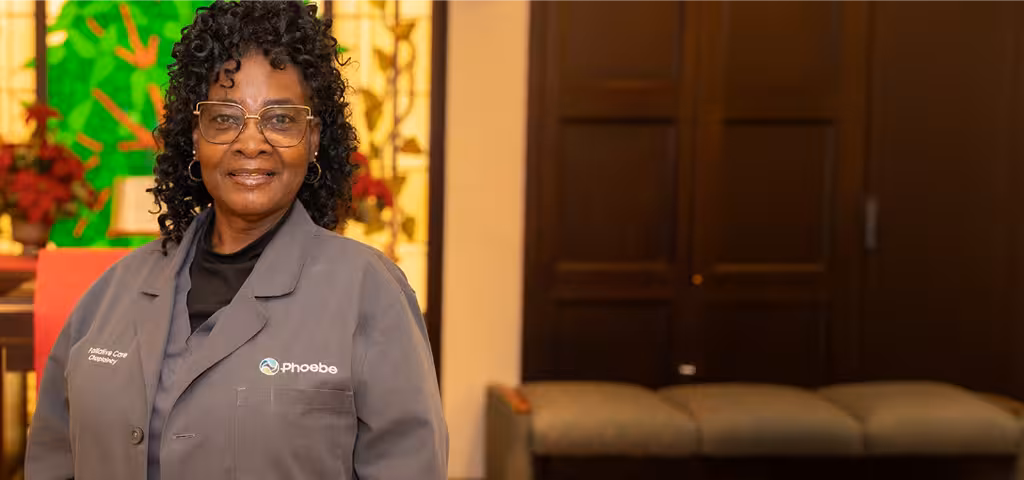 Happy Phoebe team member in a gray uniform standing in a hospital chapel decorated for the holidays.