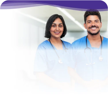 Two smiling healthcare professionals in blue scrubs with stethoscopes, standing in a brightly lit hospital hallway.