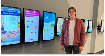 A PatientPoint employee standing next mounted tablets and smiling.