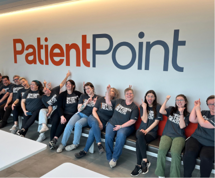 A group of PatientPoint employees sitting and pointing up to a company sign.