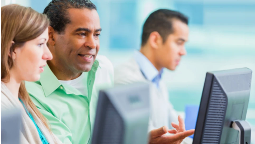 Two people discussing information while working on desktop computers.