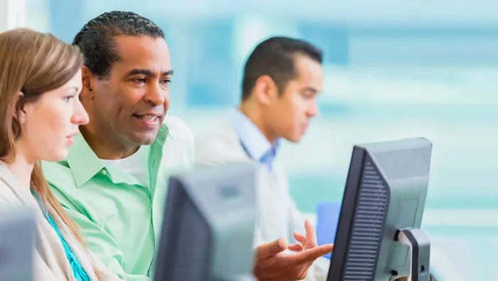 Two people discussing information while working on desktop computers.