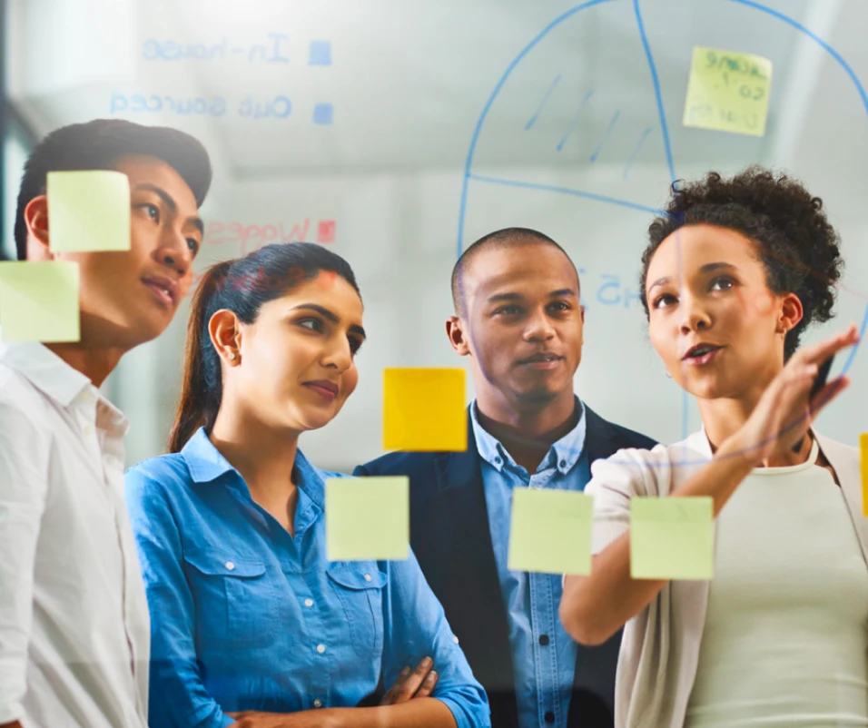 A group of employees discussing data written on a glass board.
