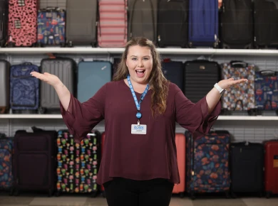 Ross retail Associate in front of carry-on luggage on display in a Ross store