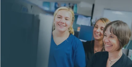 A group of smiling South Shore Health employees gathered around an office computer.
