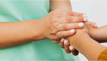 A healthcare professional holding an elderly patient’s hand.