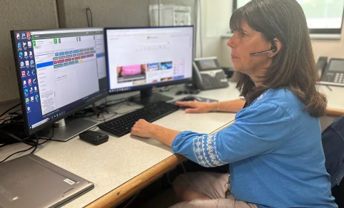An administrative working wearing a headset and sitting at a desk in front of two computer monitors.