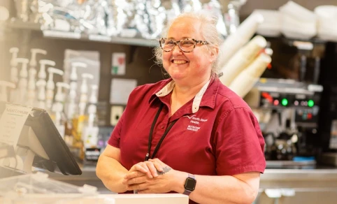 A food services employee smiling behind a café counter.