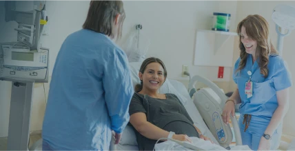 Two nurses assisting and laughing with a patient in a hospital bed.