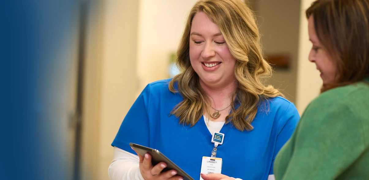 A TriHealth nurse next to a patient pointing at digital tablet.