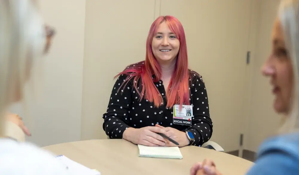 Social worker with pink hair smiling during a conversation at a table