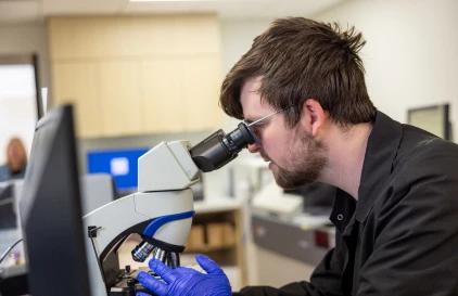 A UC Health employee looking through a microscope.