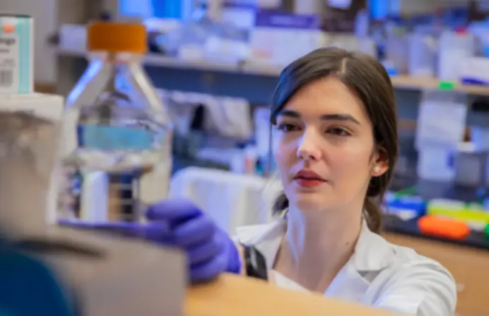 A female lab worker reaches for a bottle off the shelf in the lab.