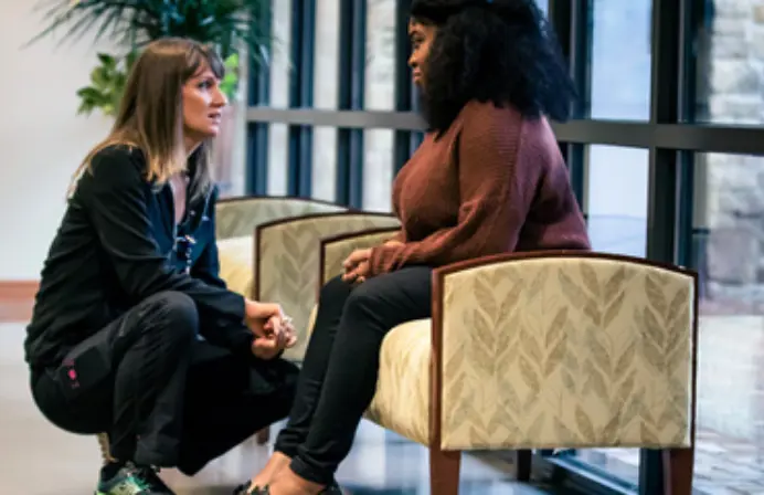  	A female social worker talks to seated female client in the lobby of the hospital.