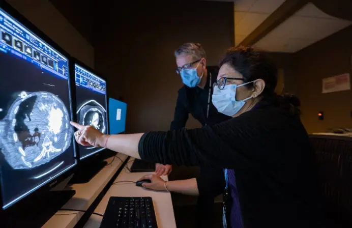 An older male radiologist and a younger male intern study results at a computer screen.