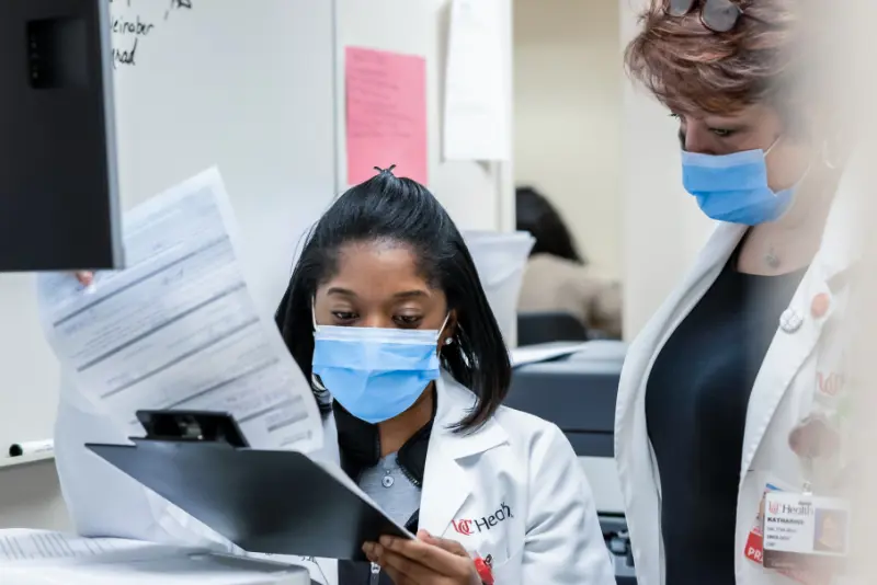  	Two female nurses study a computer screen about a patient’s progress. 