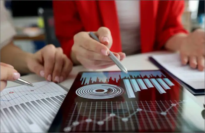 A hand holding a pen over some papers that feature graphs and charts.