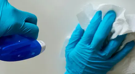 Hands with blue gloves and a spray bottle cleaning a surface.