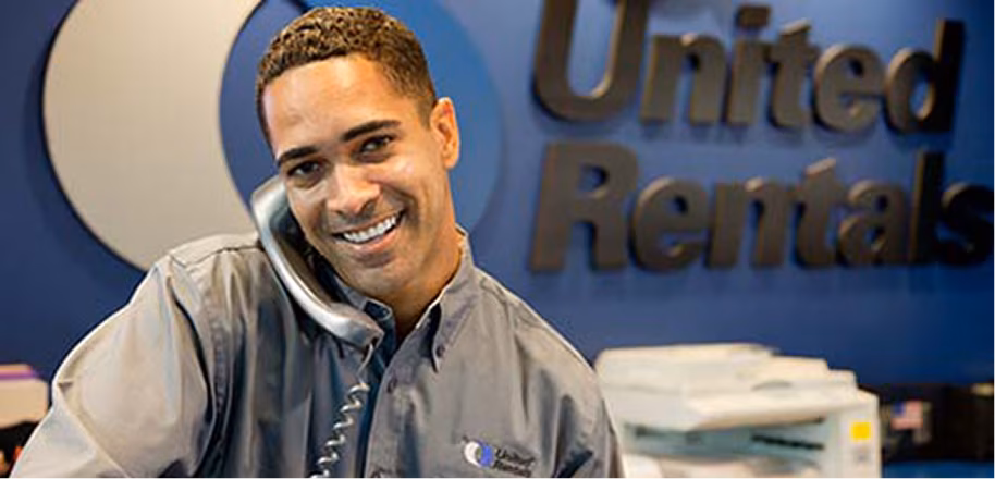 A United Rentals employee smiling while holding a hard hat.