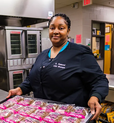 A team member smiling and holding a tray of food in a cafeteria.