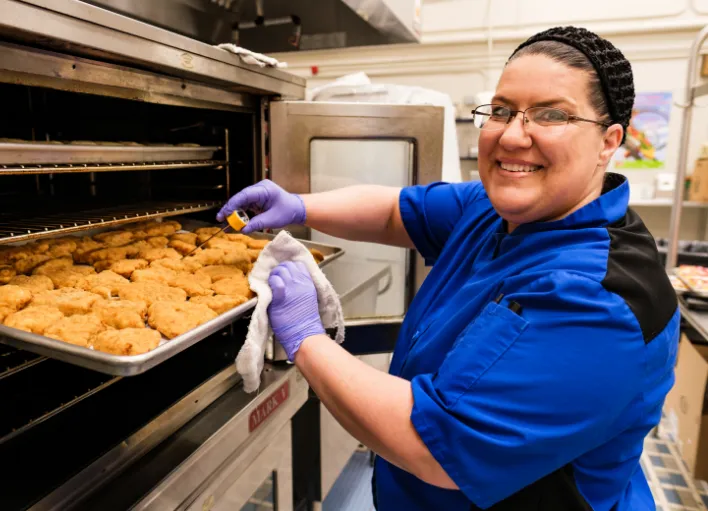 An employee of the nutrition team checking on some food in the oven.