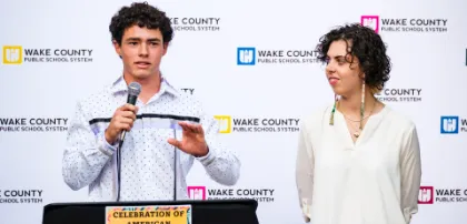 A Wake County teacher standing next to a student speaking at a seminar.