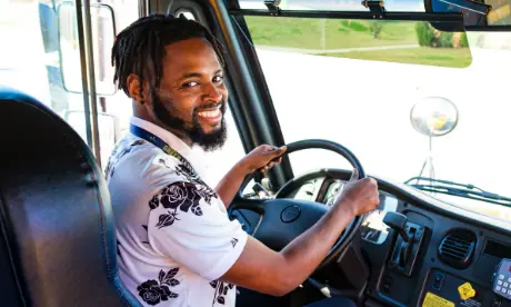 A bus driver sitting in a bus and smiling.