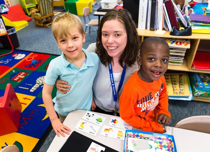 A Special Education Instructional Assistant hugging two students.