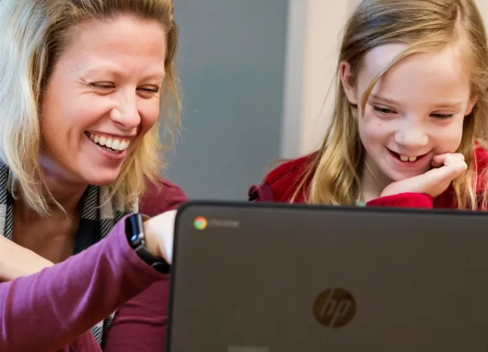 A substitute teacher helping a student on a laptop assignment.