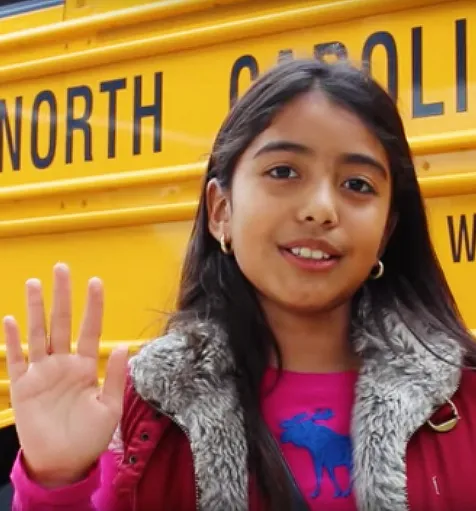 Student waves outside a yellow school bus.