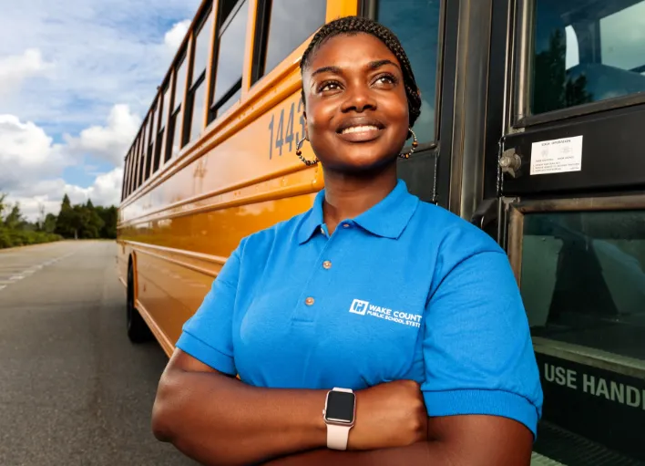 Smiling bus driver standing outside of her bus at Wake County Public School System.