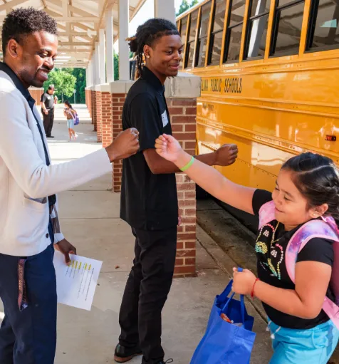 A student giving fist bumps to two Wake County safety assistants.