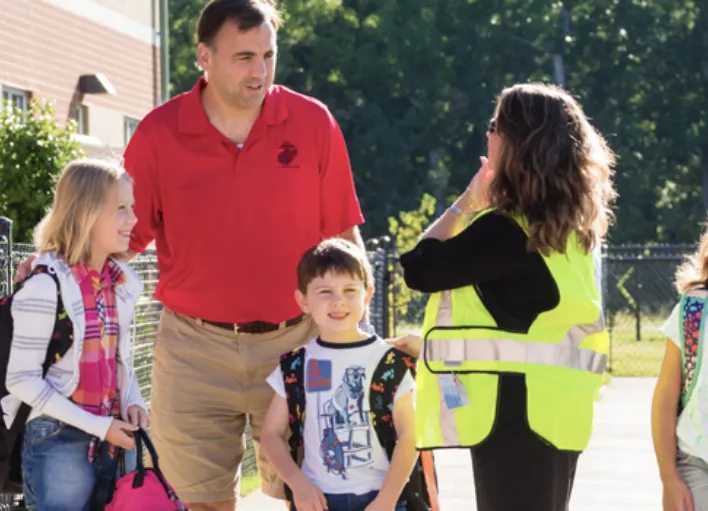 A parent and two students talking to a bus safety assistant.