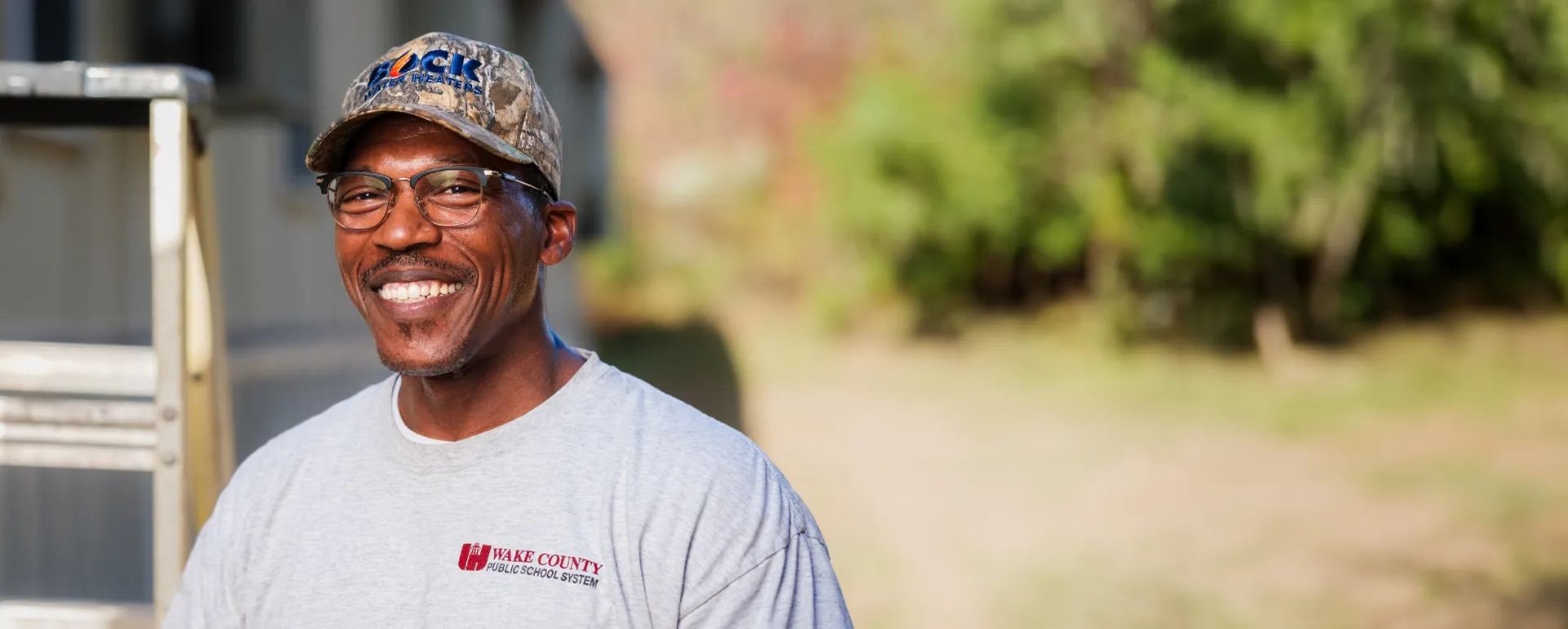 Smiling maintenance technician standing with a ladder.