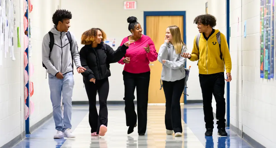 Four students walking and conversing with a leader in a hallway.