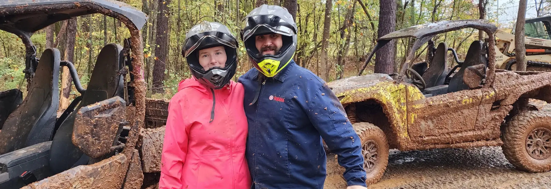 Two Yamaha employees in helmets pose next to a dirt bike track in a forest.