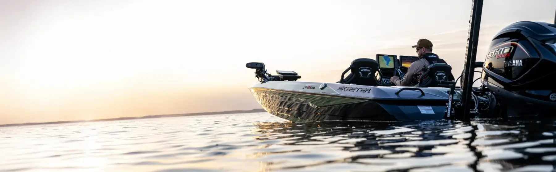 A person in a Skeeter fishing boat watching the sun set over the water.