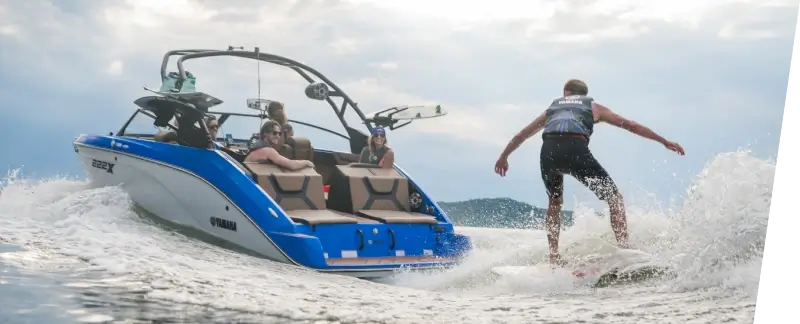 A person wakeboarding behind a Yamaha jet boat on a lake.