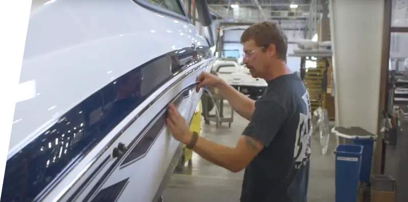 A Yamaha employee adding a decal sticker to a boat on the manufacturing floor.