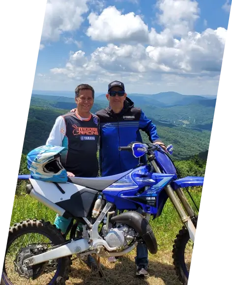 Two people standing next to a Yamaha offroad motorcycle on a mountain track.