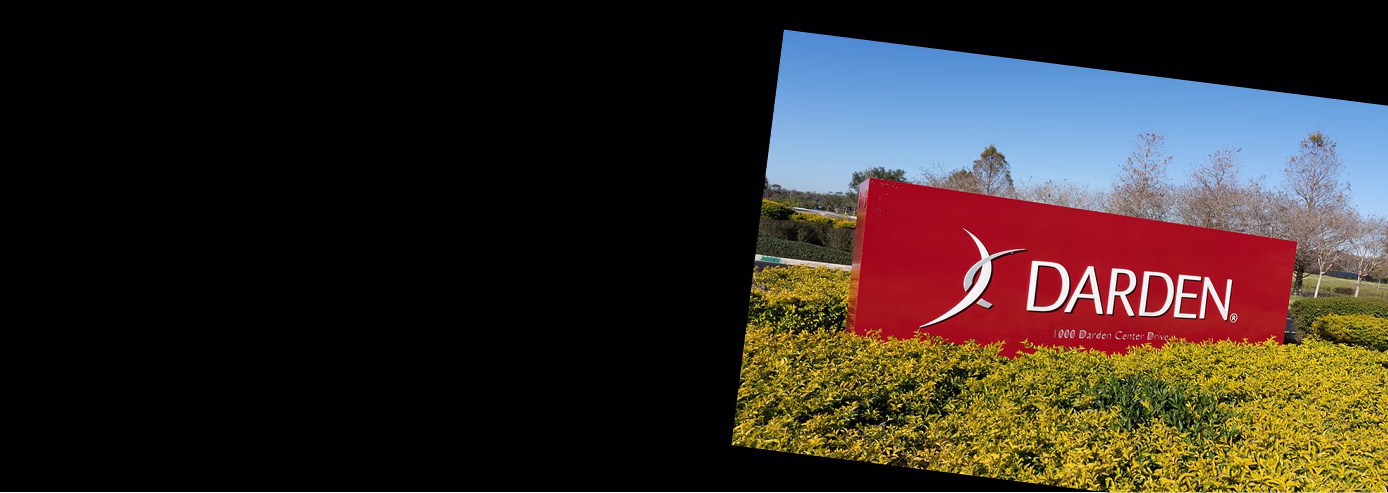 A Darden corporate sign in the middle of a green bush.