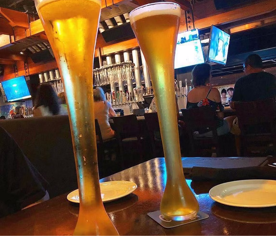 Two tall glasses of freshly poured beer sitting on a table.