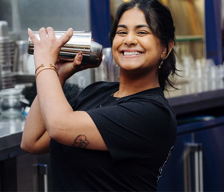 A smiling bartender shaking up a mixed drink.