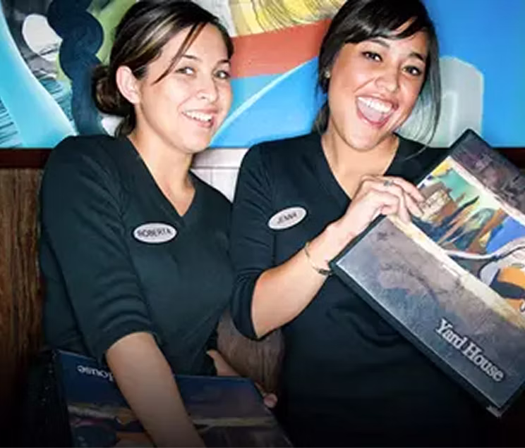 Two female hosts, smiling and holding a menu by the entrance.