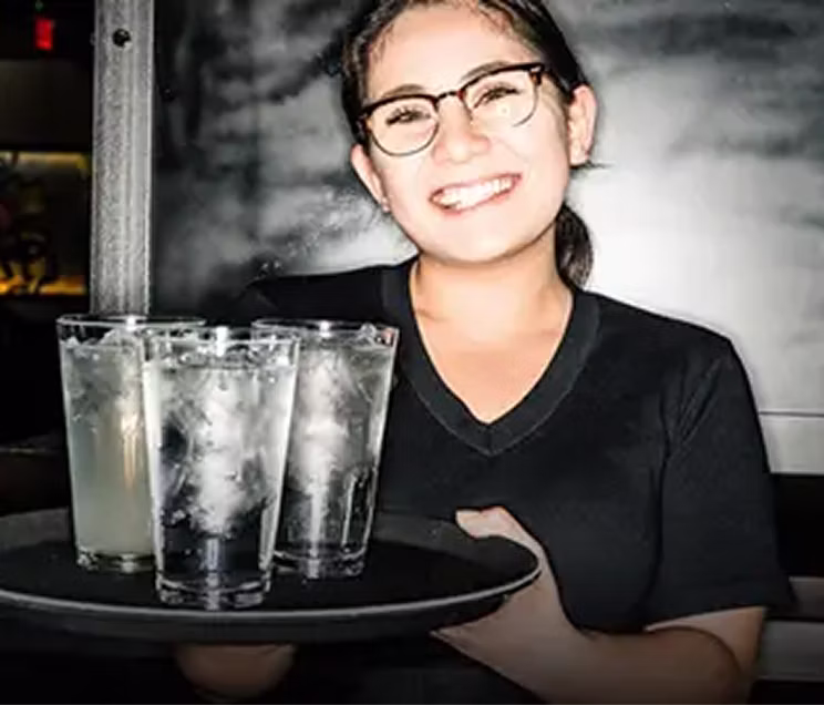 A smiling server holding a tray of water glasses.